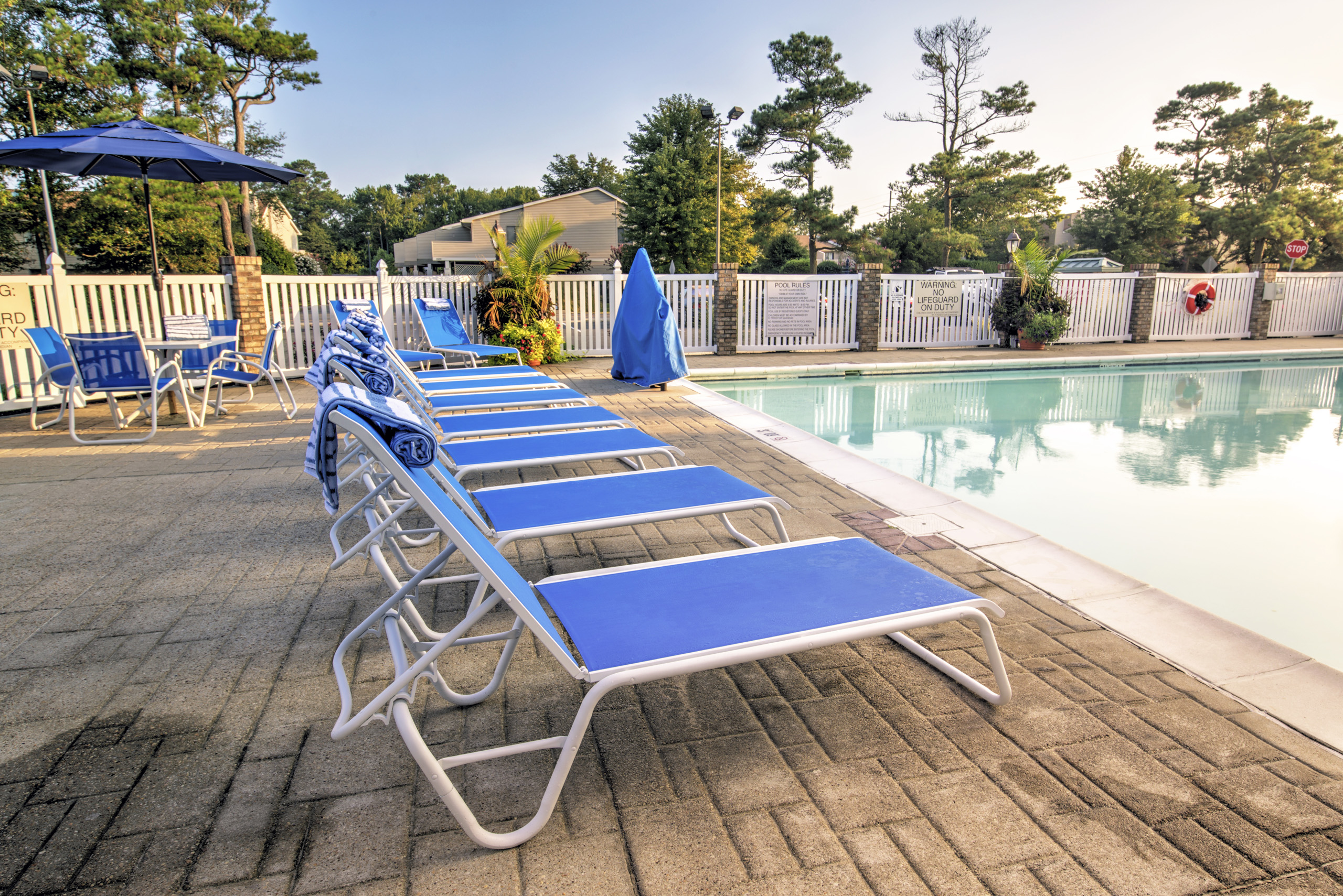 Poolside lounge chairs lined up beside calm water.