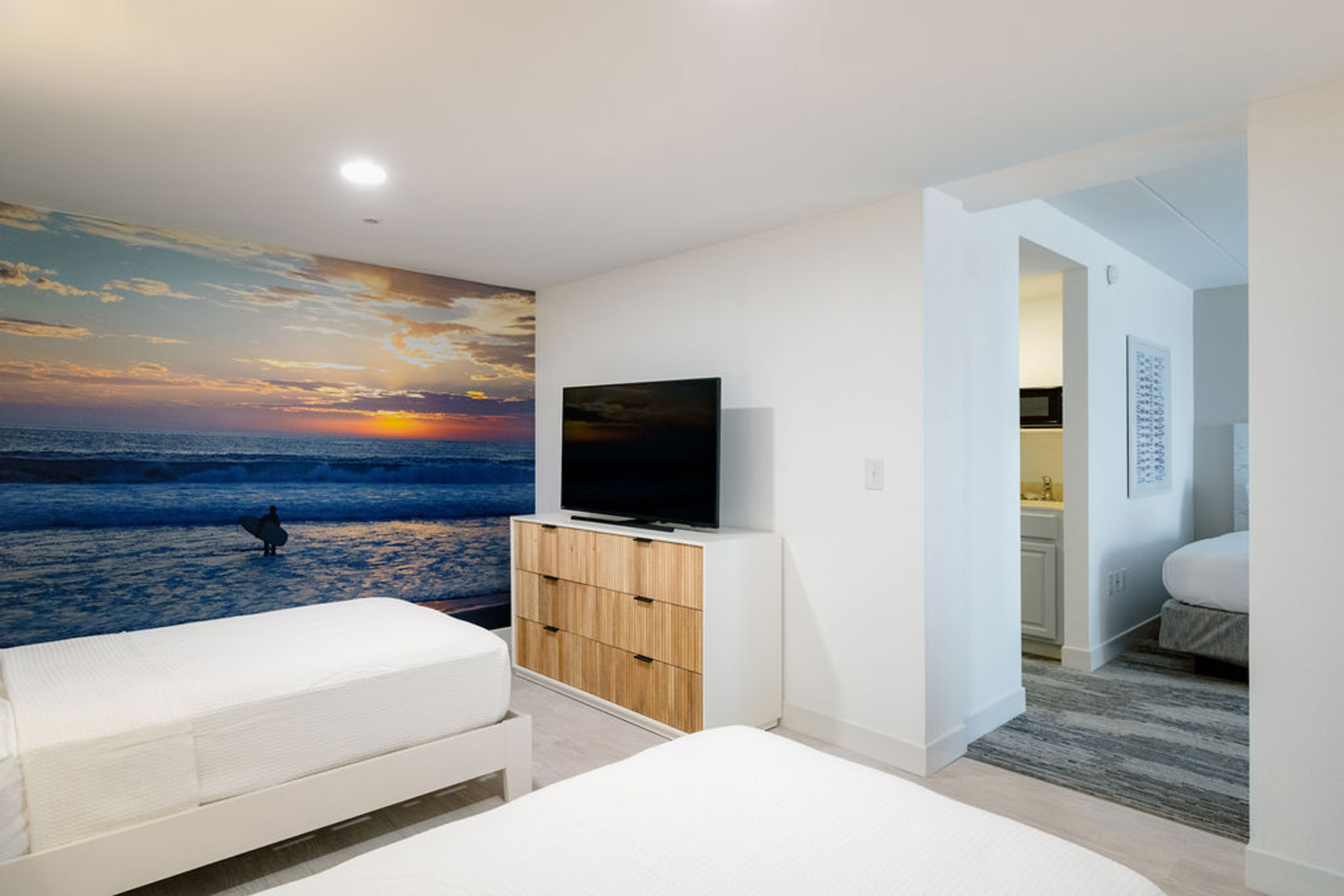 Bedroom with ocean sunset mural and TV dresser.