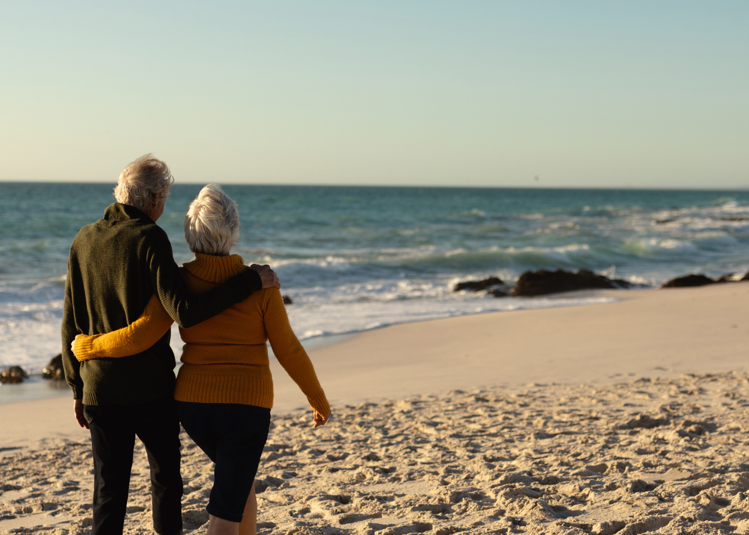 Older couple walking along peaceful beach shoreline.