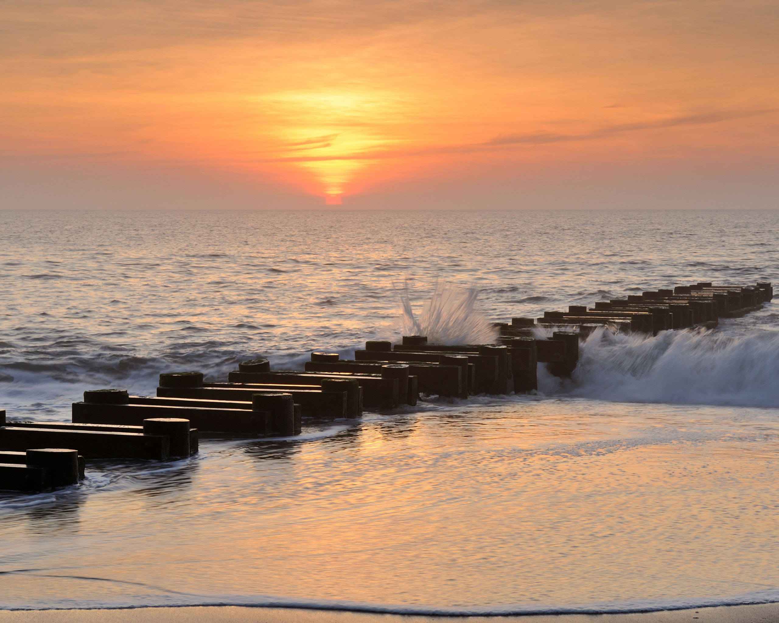 Ocean pier at sunrise with waves crashing.