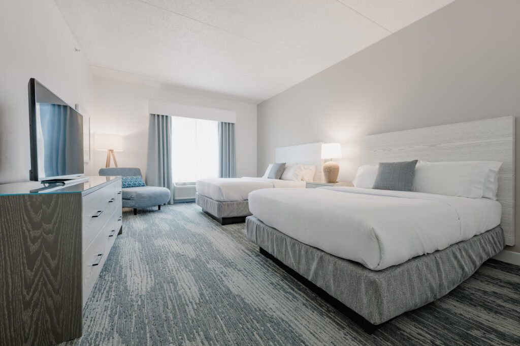 Modern hotel room with two beds and TV.