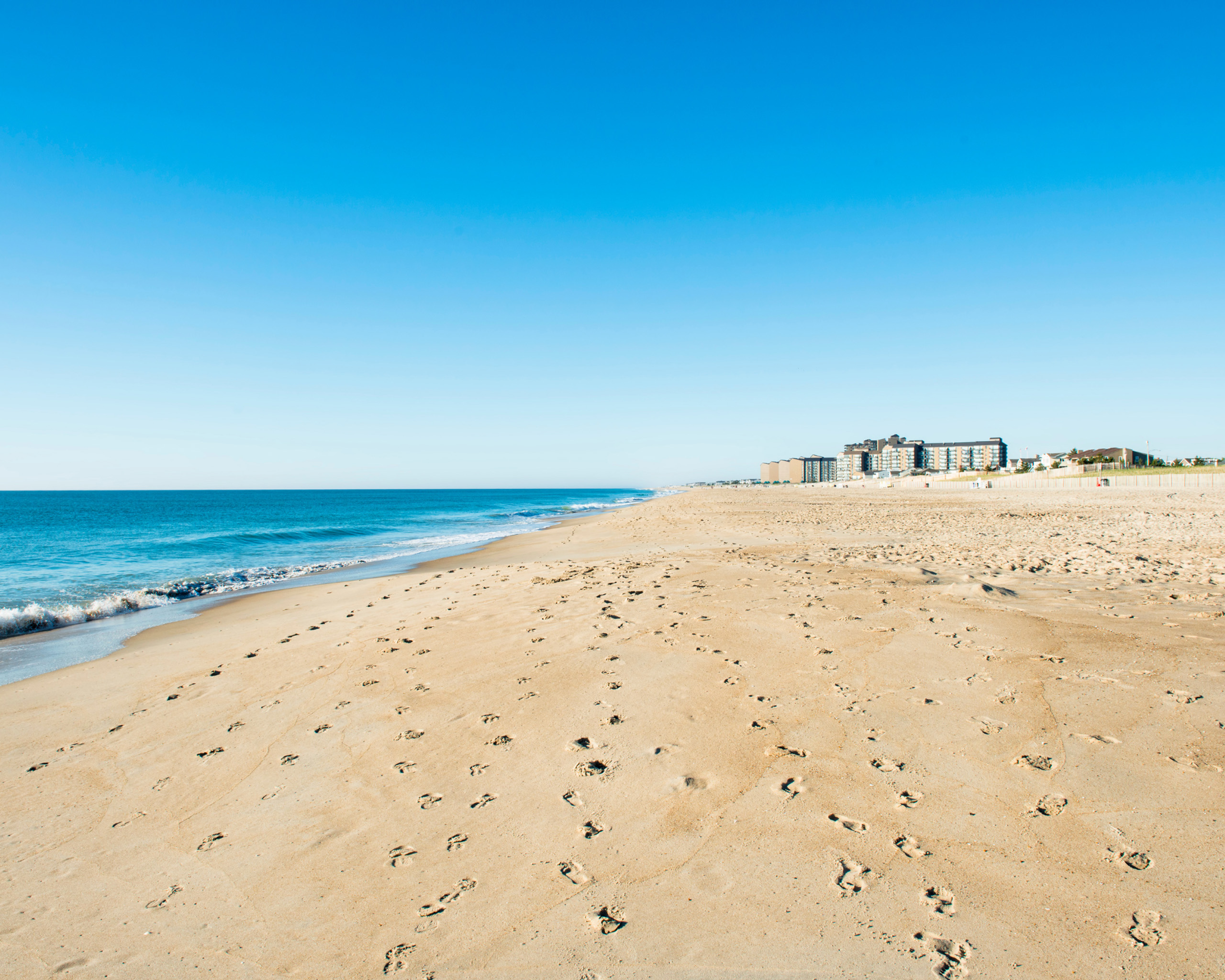 Wide sandy beach with ocean and distant buildings.