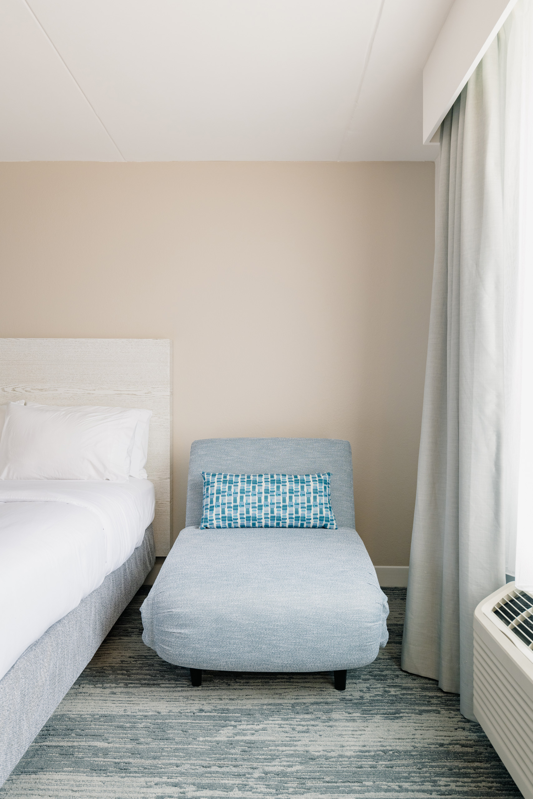 Blue lounge chair beside bed and window.