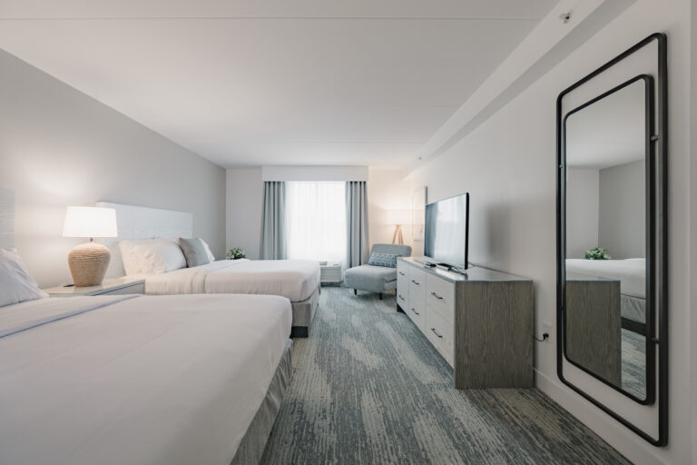 Two-queen room with TV, mirror, and window view.