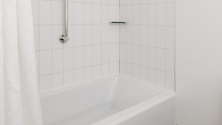 White tiled bathtub with grab bar and shower curtain.