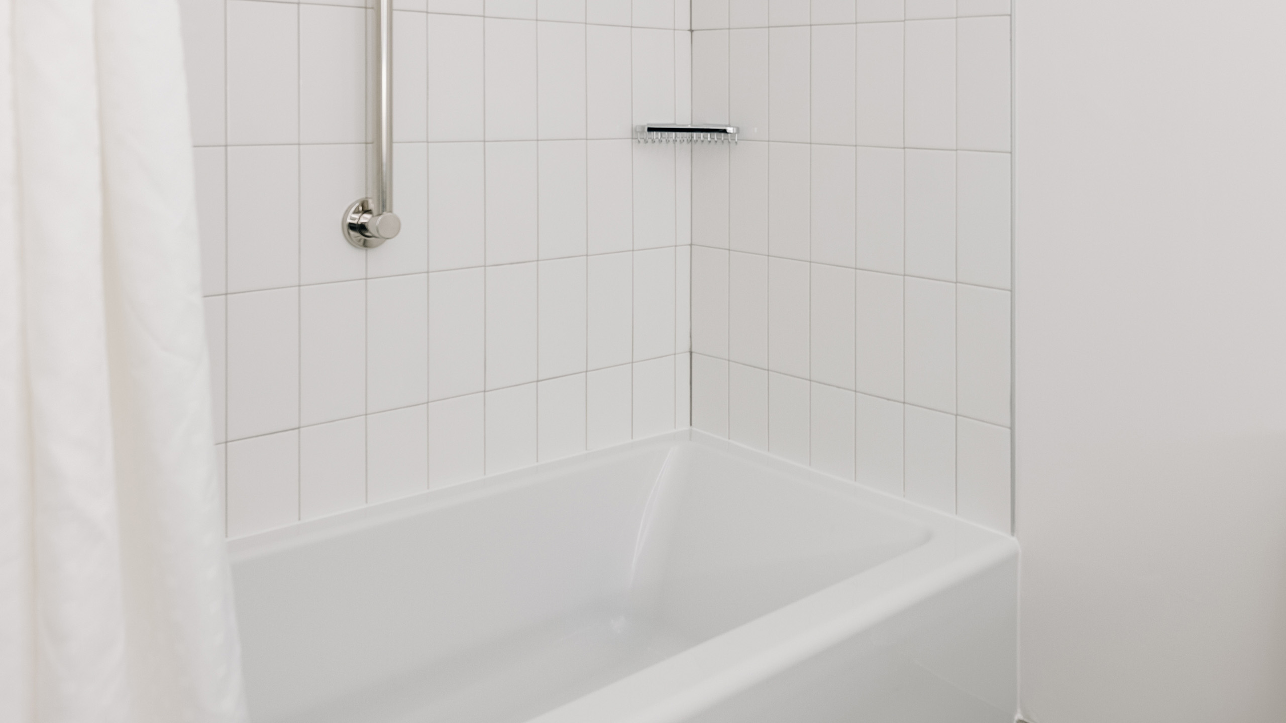 White tiled bathtub with grab bar and shower curtain.