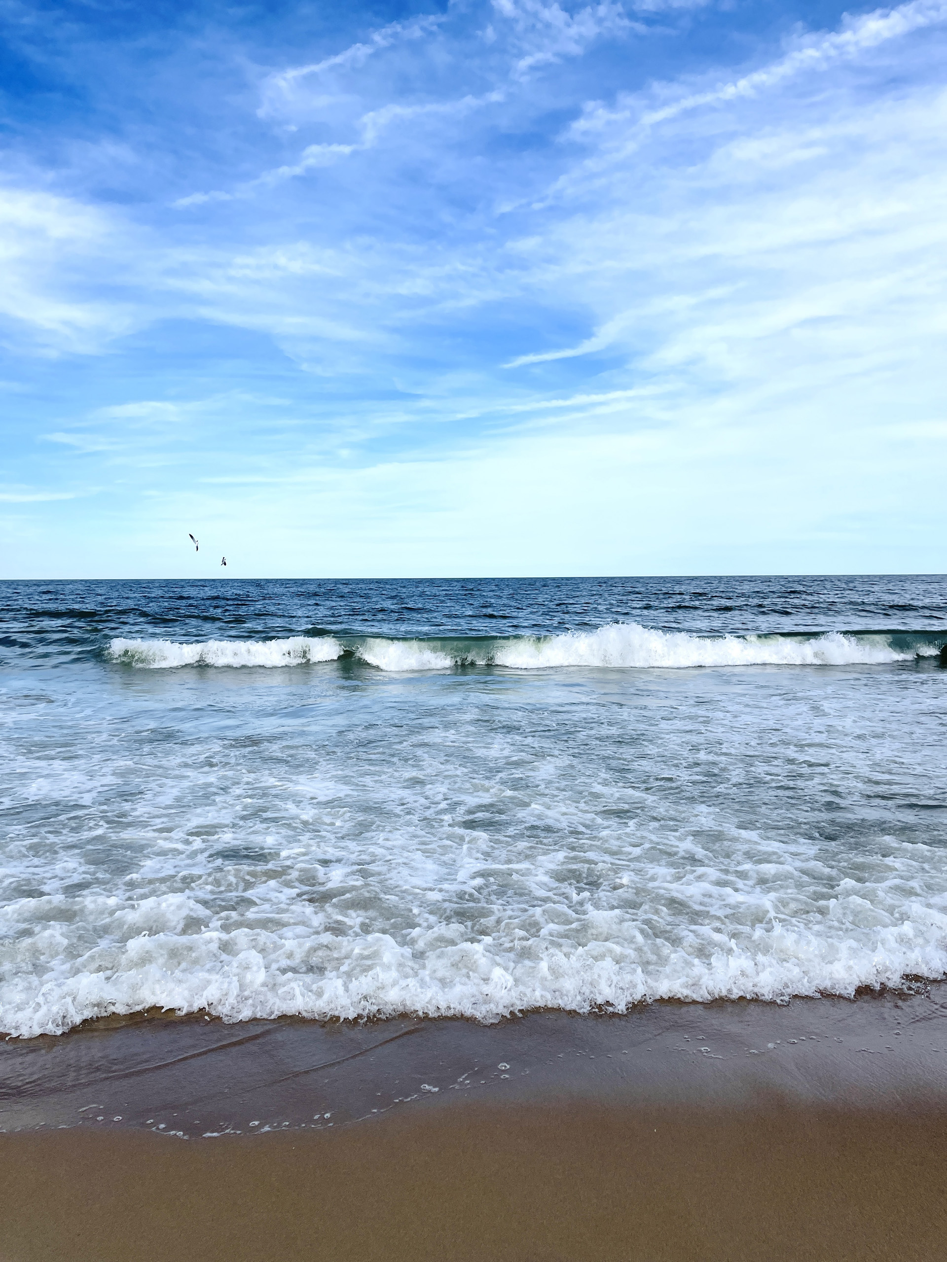 Waves rolling onto sandy beach under a bright blue sky.