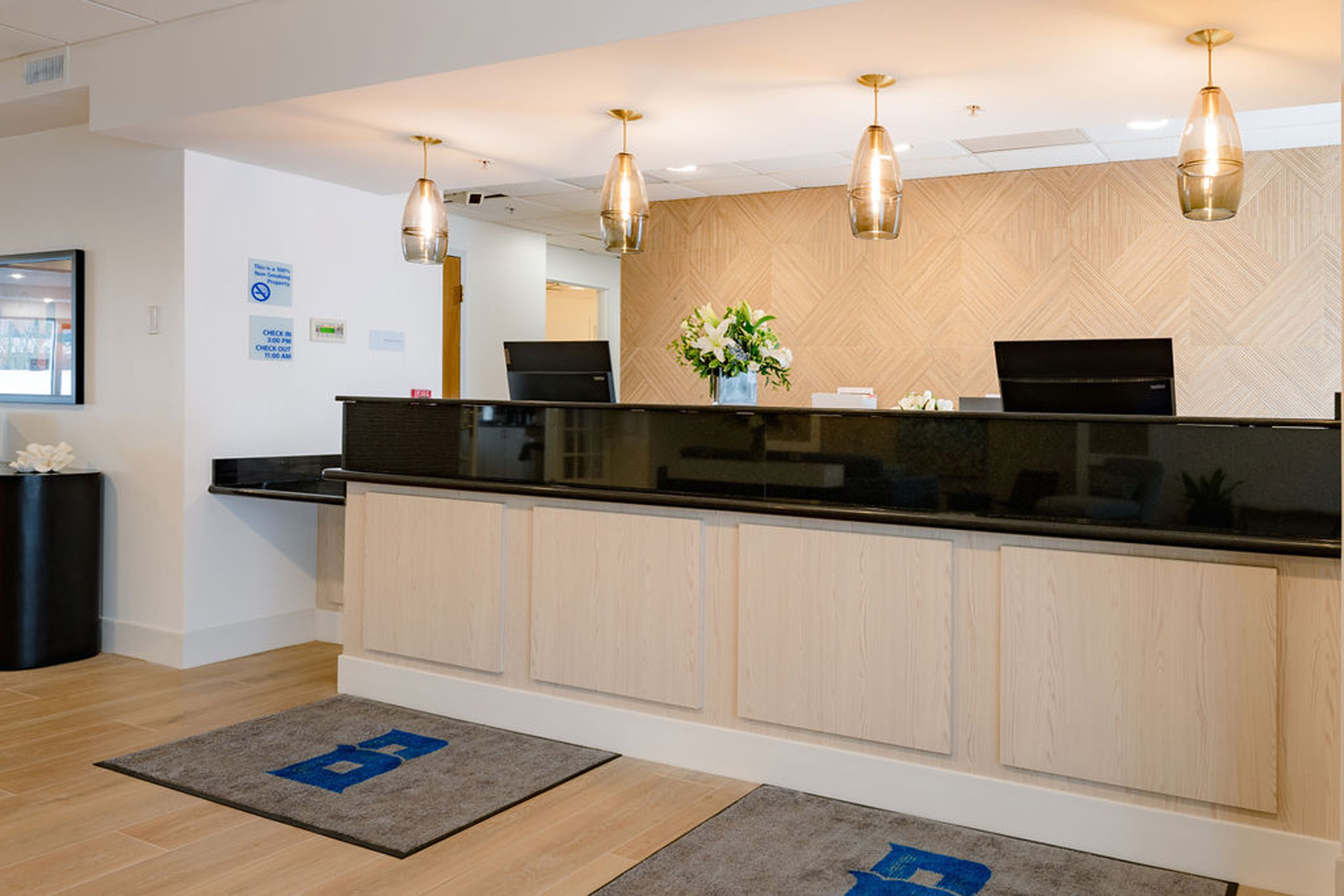 Modern hotel reception desk with light wood panels, black counter, and hanging pendant lights.