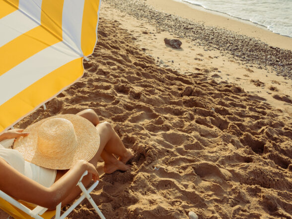 Person relaxing under yellow umbrella on sandy beach.