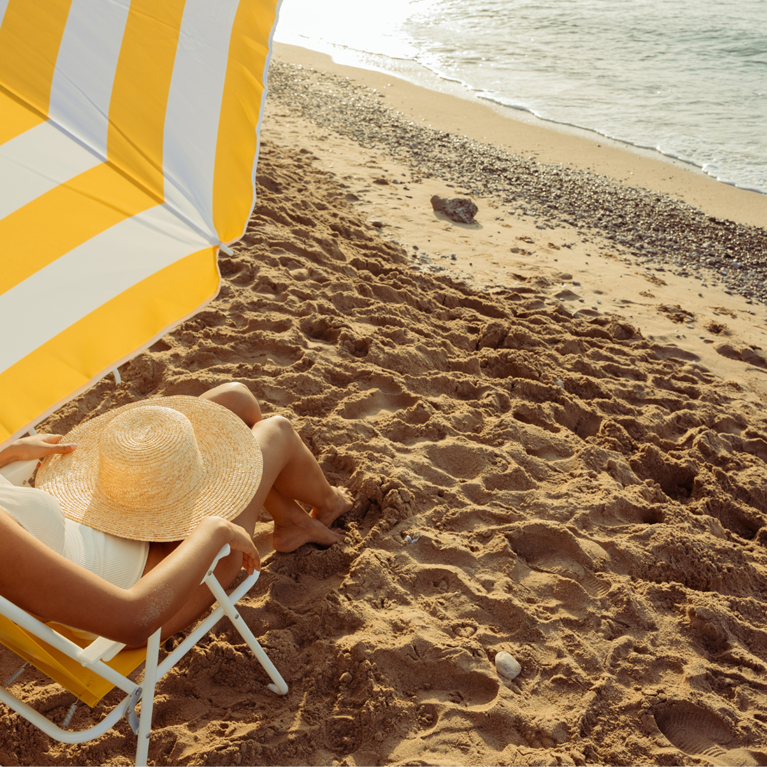 Person relaxing under yellow umbrella on sandy beach.