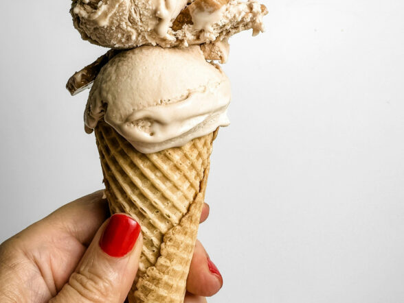 Hand holding waffle cone with two scoops of ice cream.