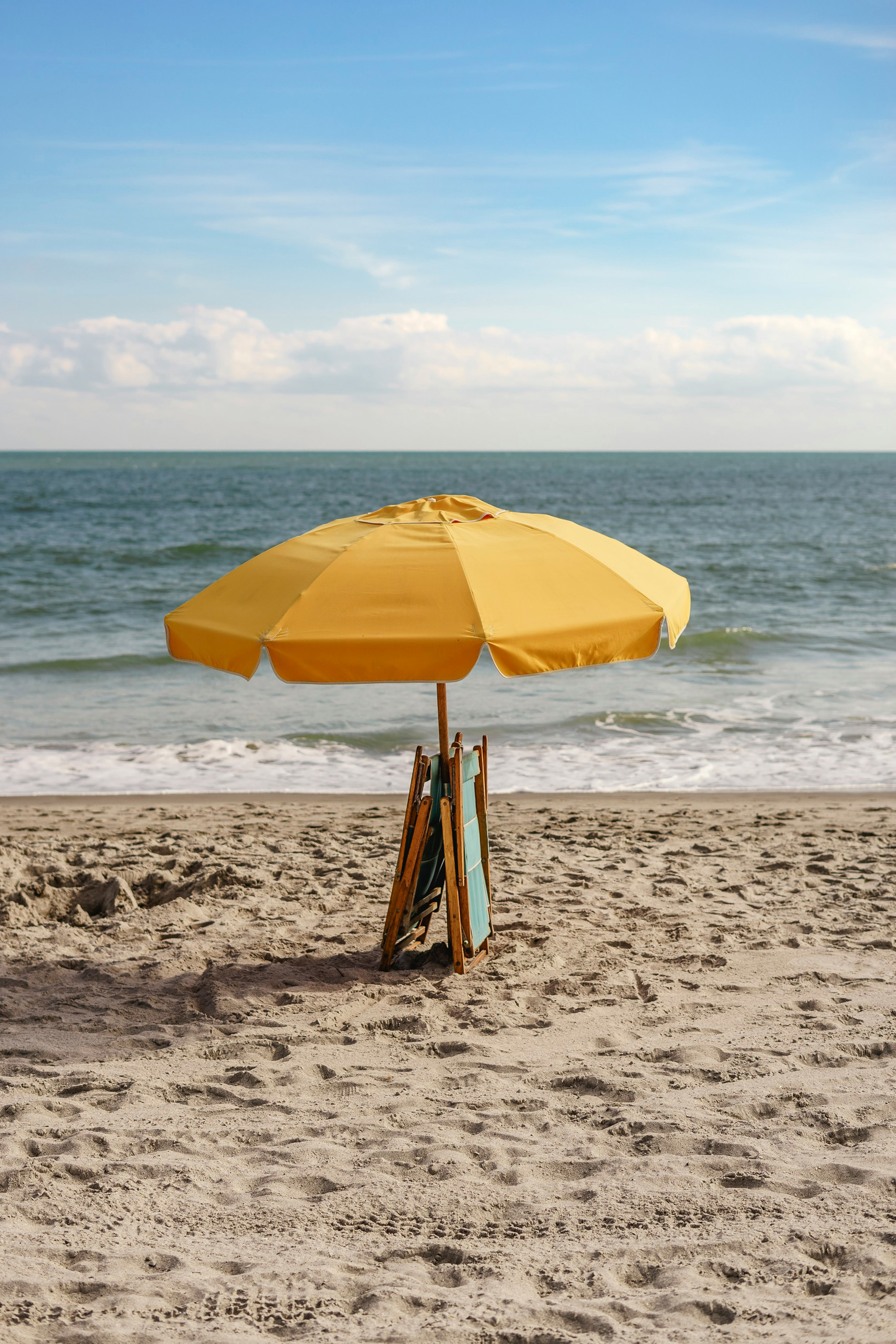 Bright yellow beach umbrella with folded chairs by the sea.
