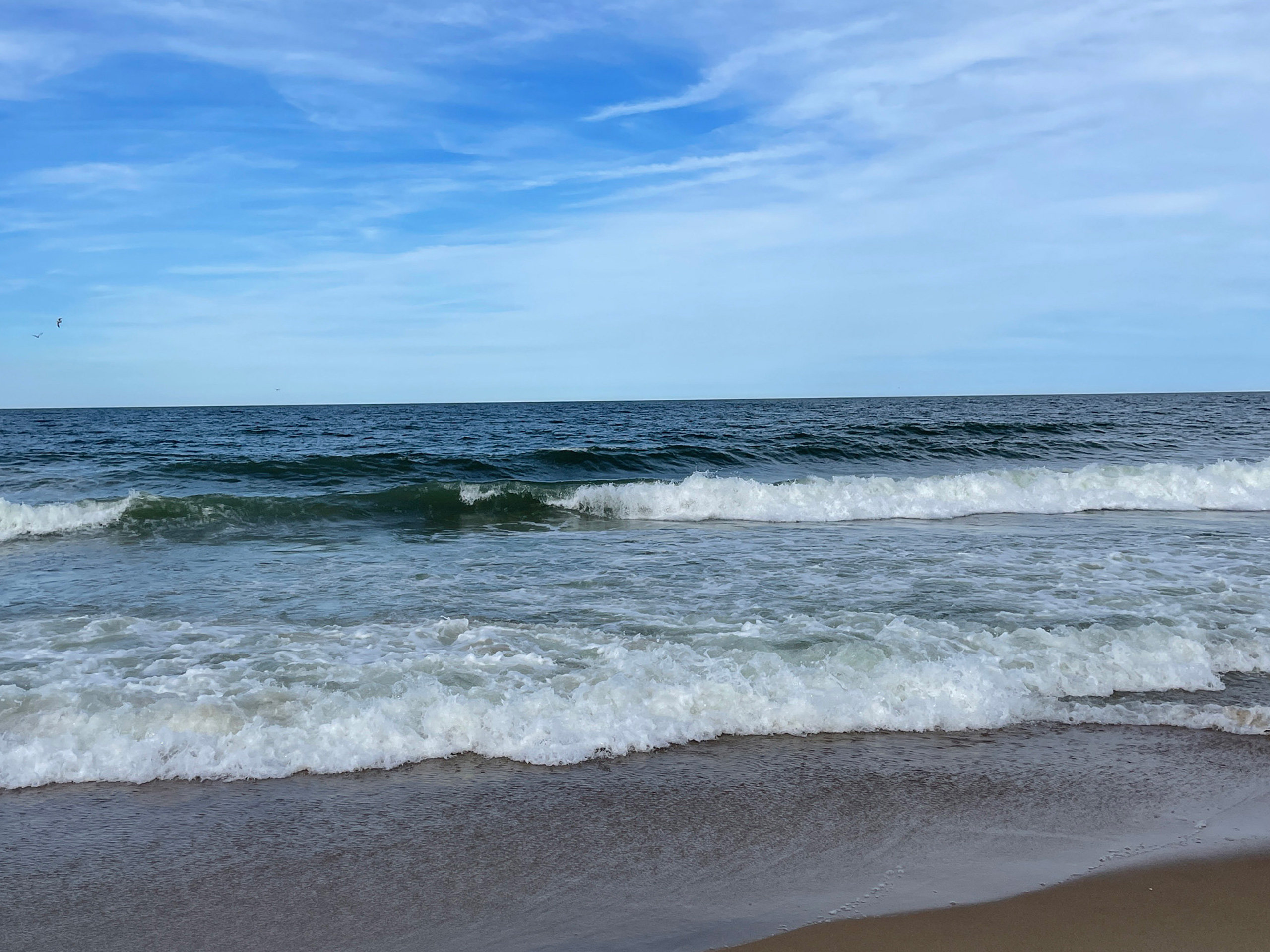 Ocean waves meeting sandy beach under blue sky.